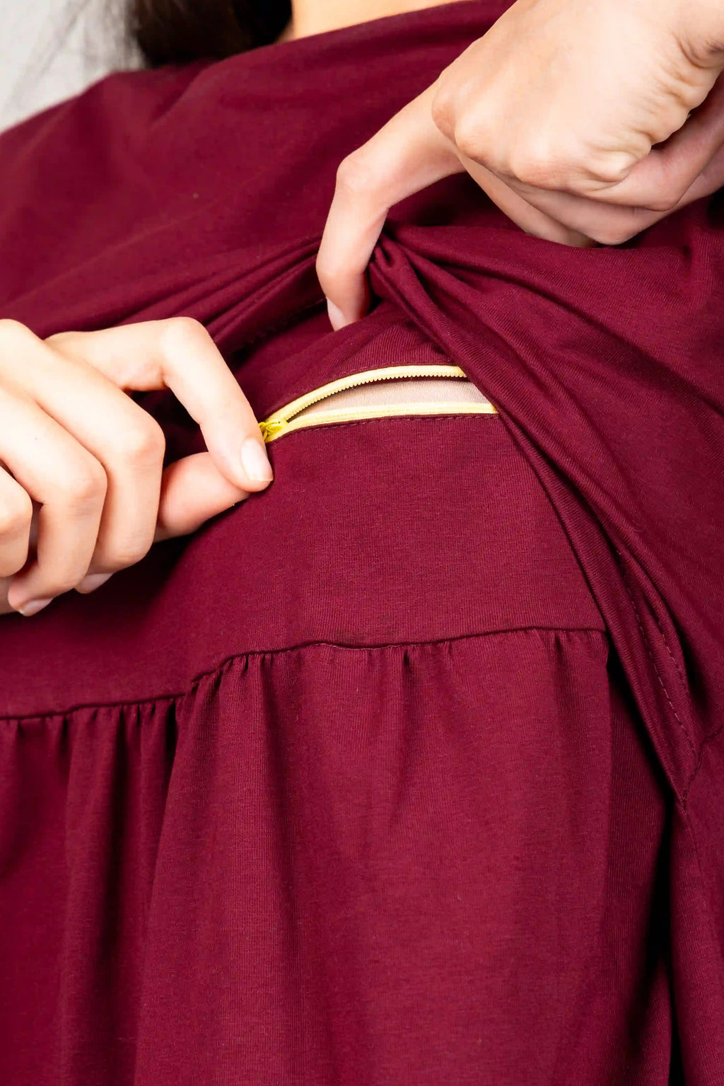 Close-up of a person wearing a burgundy dress and lifting the sleeve to reveal a built-in gold zipper pocket.