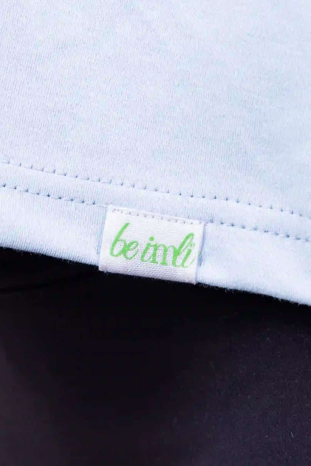 Close-up of a light blue top with a small green and white 'be imli' brand tag near the hem, worn with dark leggings.