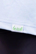 Close-up of a light blue top with a small green and white 'be imli' brand tag near the hem, worn with dark leggings.
