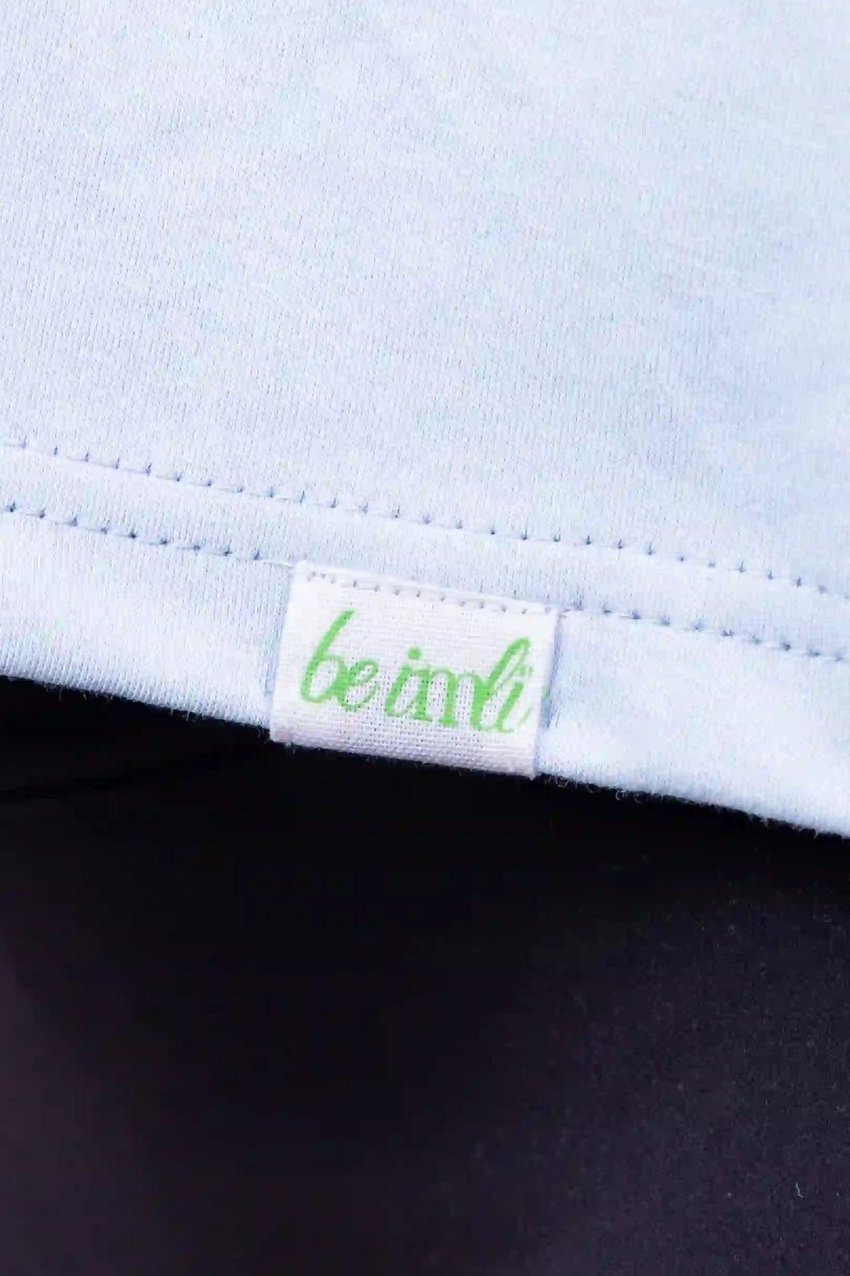 Close-up of a light blue top with a small green and white 'be imli' brand tag near the hem, worn with dark leggings.