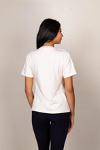 A woman viewed from the back wearing a plain white short-sleeve crewneck t-shirt and dark navy leggings, standing against a neutral beige studio background.